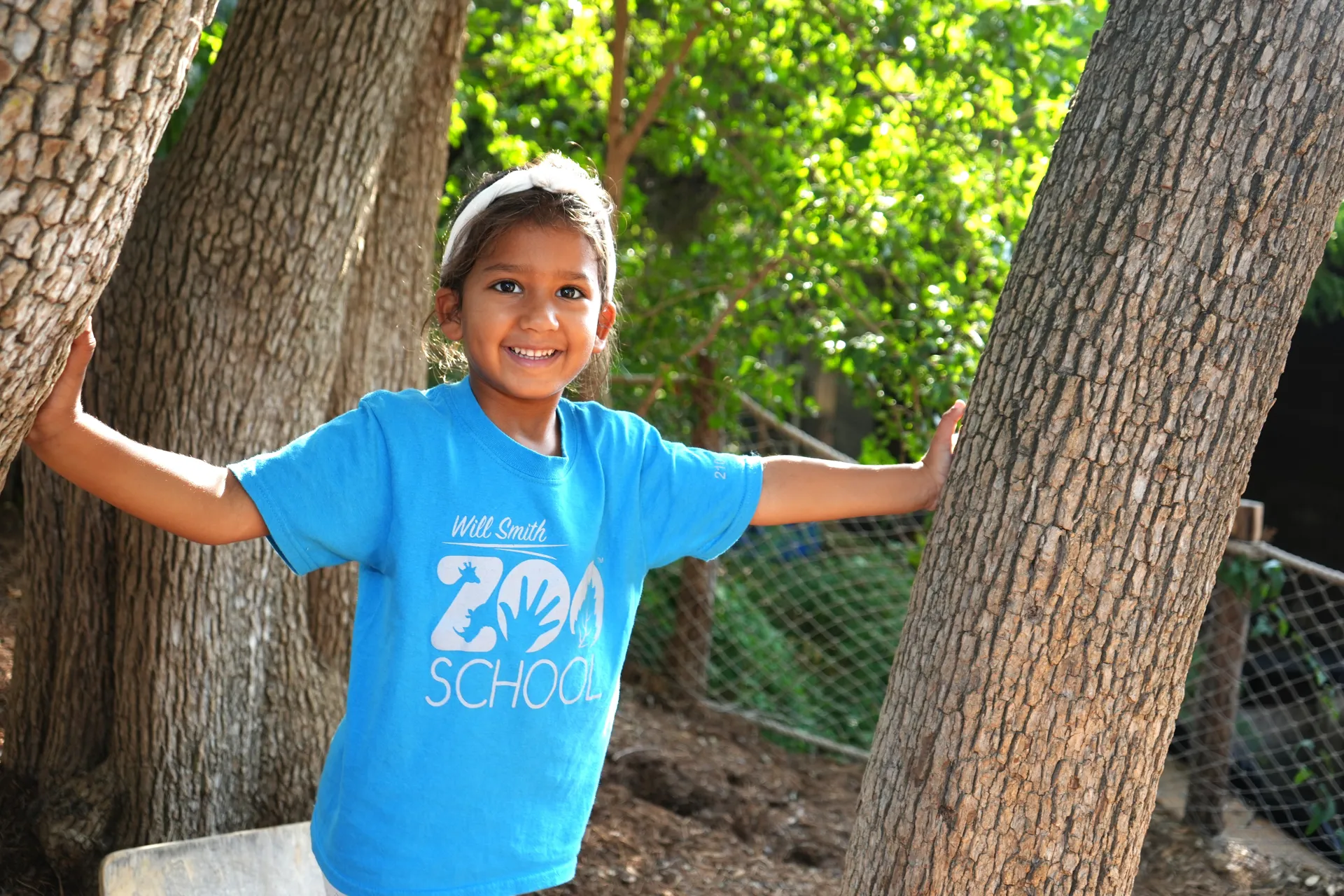 A girl with her arms outstretched and resting on two tree trunks