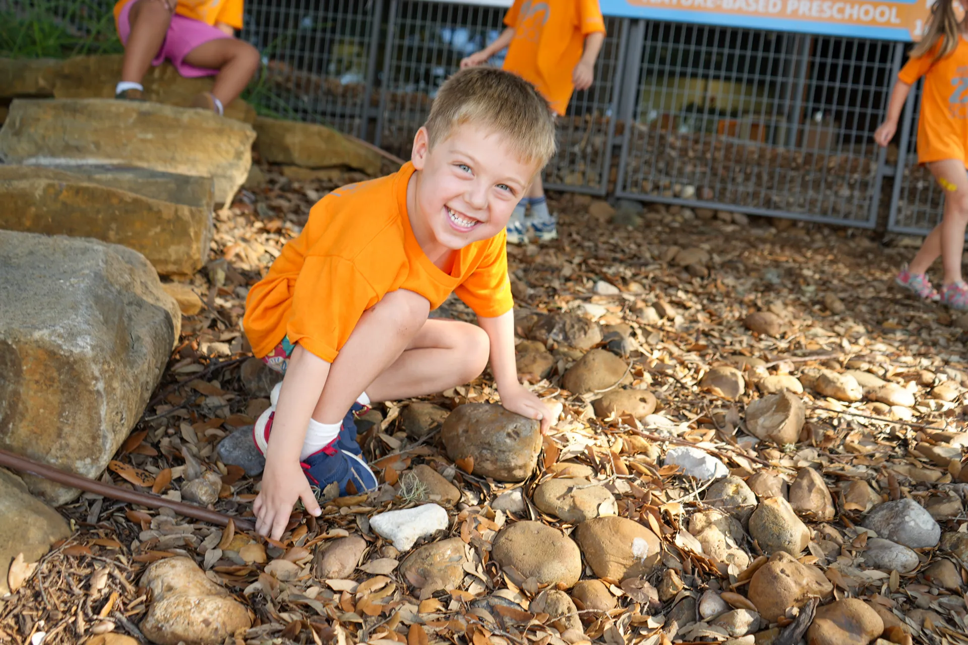 Boy kneeling down smiling with two children walking in the background
